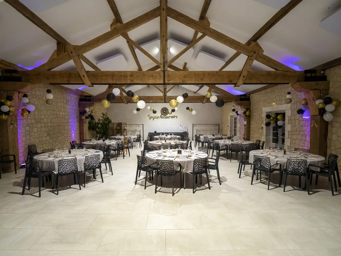 Salle de réception dressée avec tables rondes et charpente apparente